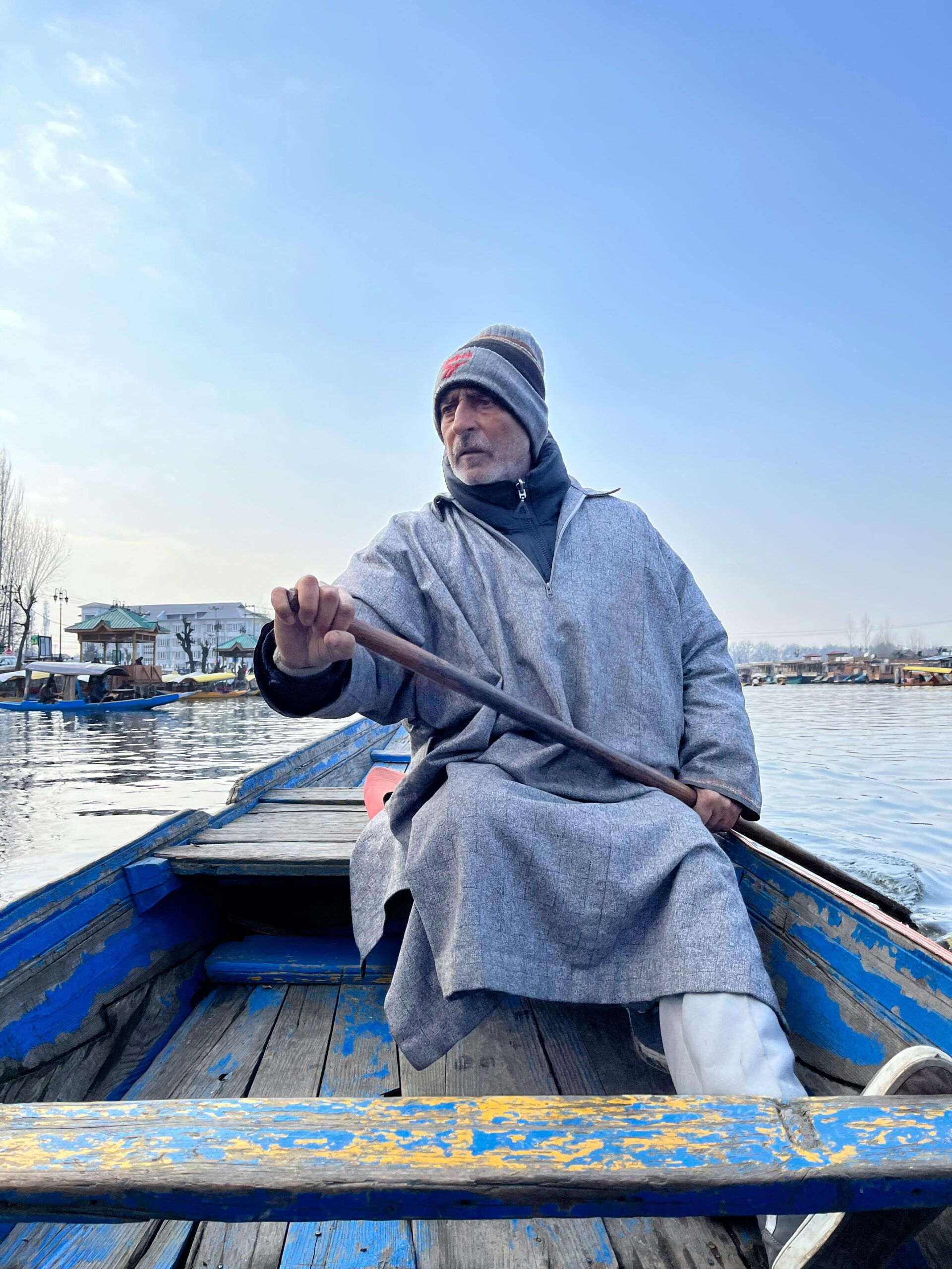 An elderly man rowing a traditional boat on Dal Lake, Srinagar on a clear day.